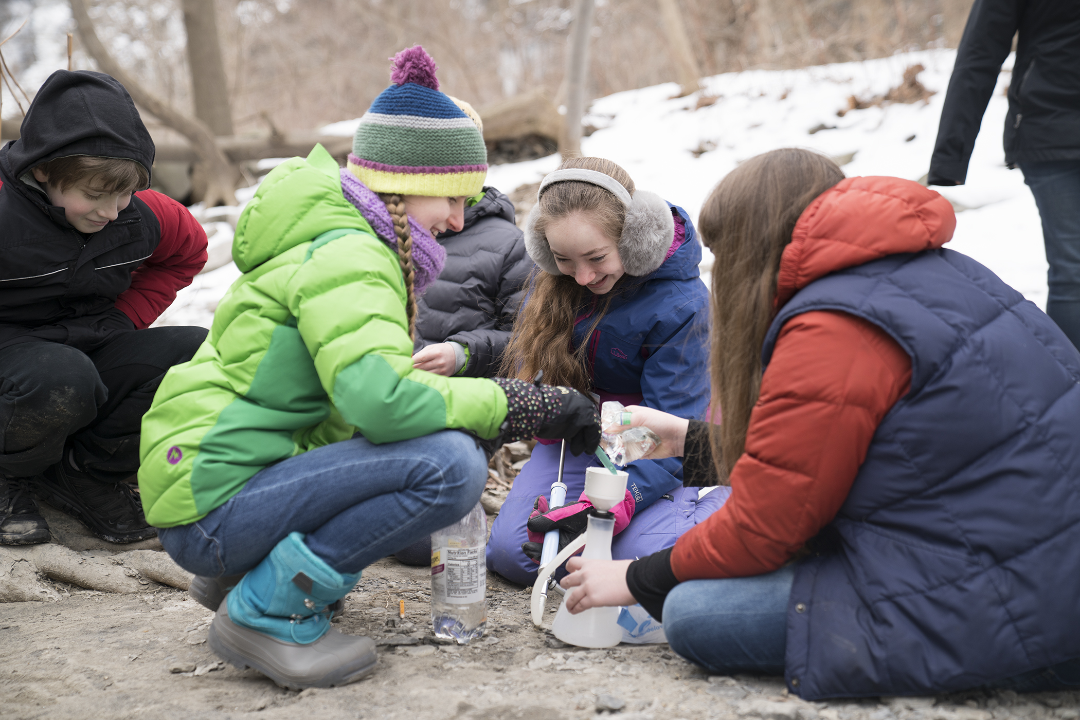 Students crouching on ground in the winter pouring water into a container