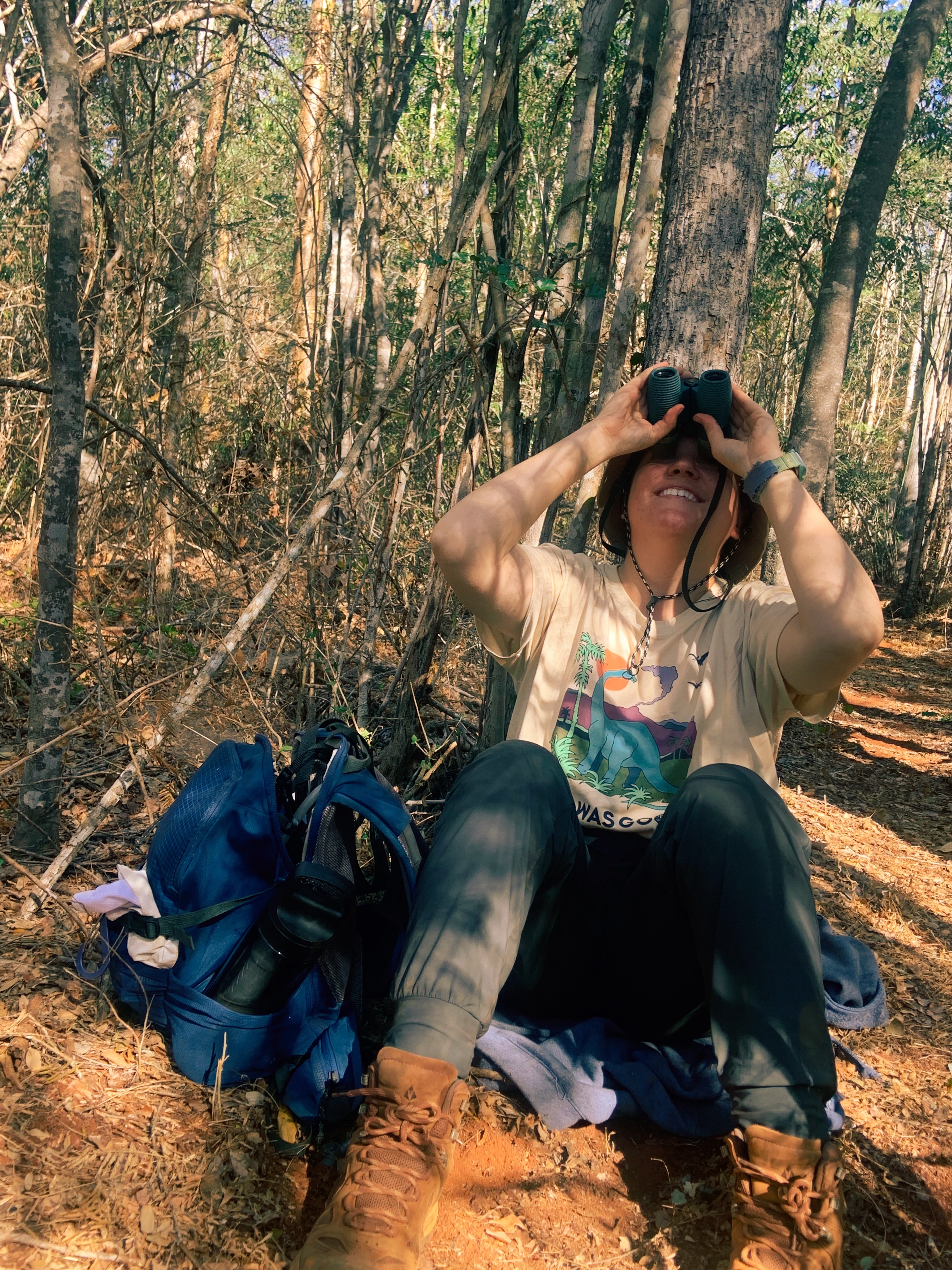 Shayna sitting in the woods, looking through binoculars.