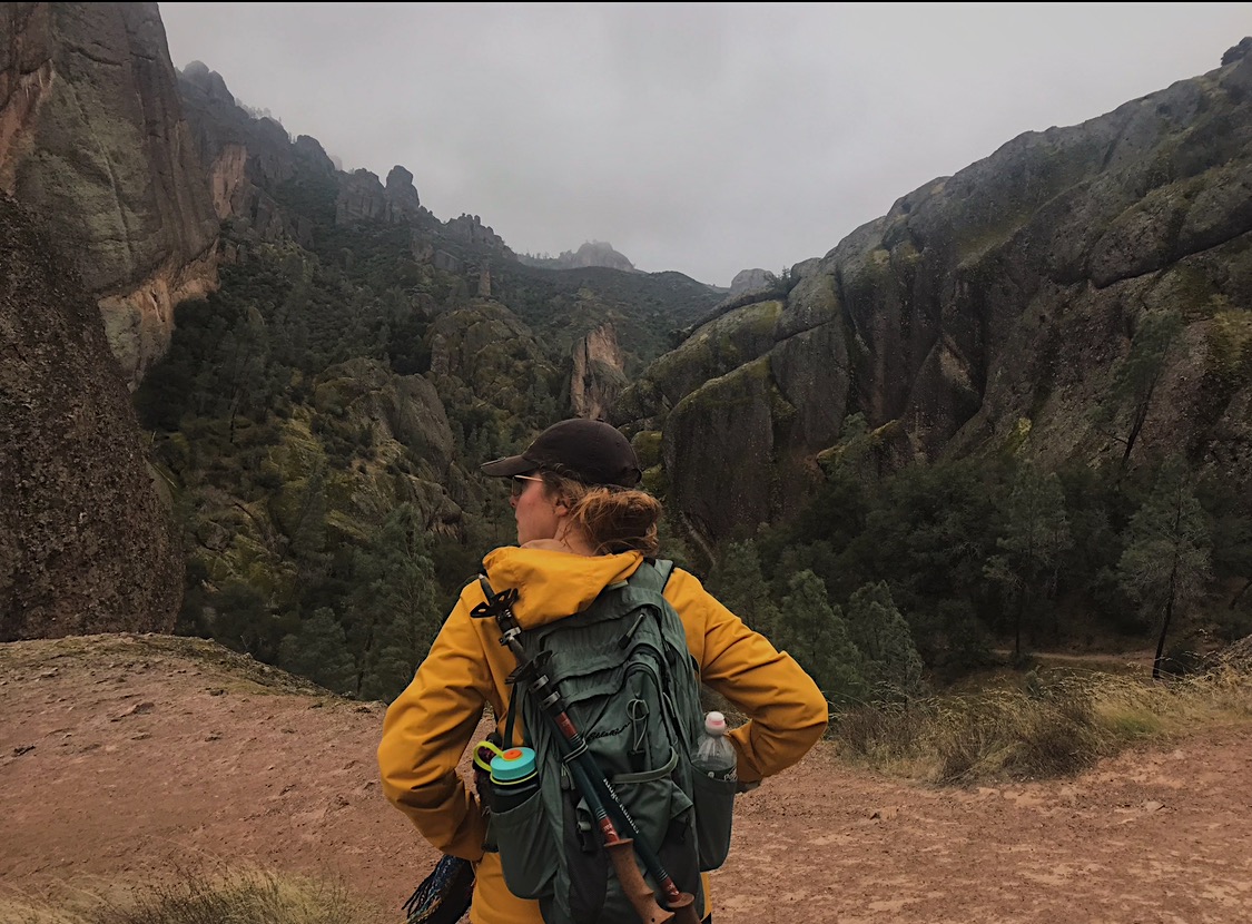 Amanda is looking off into the distance, with her back to the camera. There are mountains in front of her as she looks to the left.