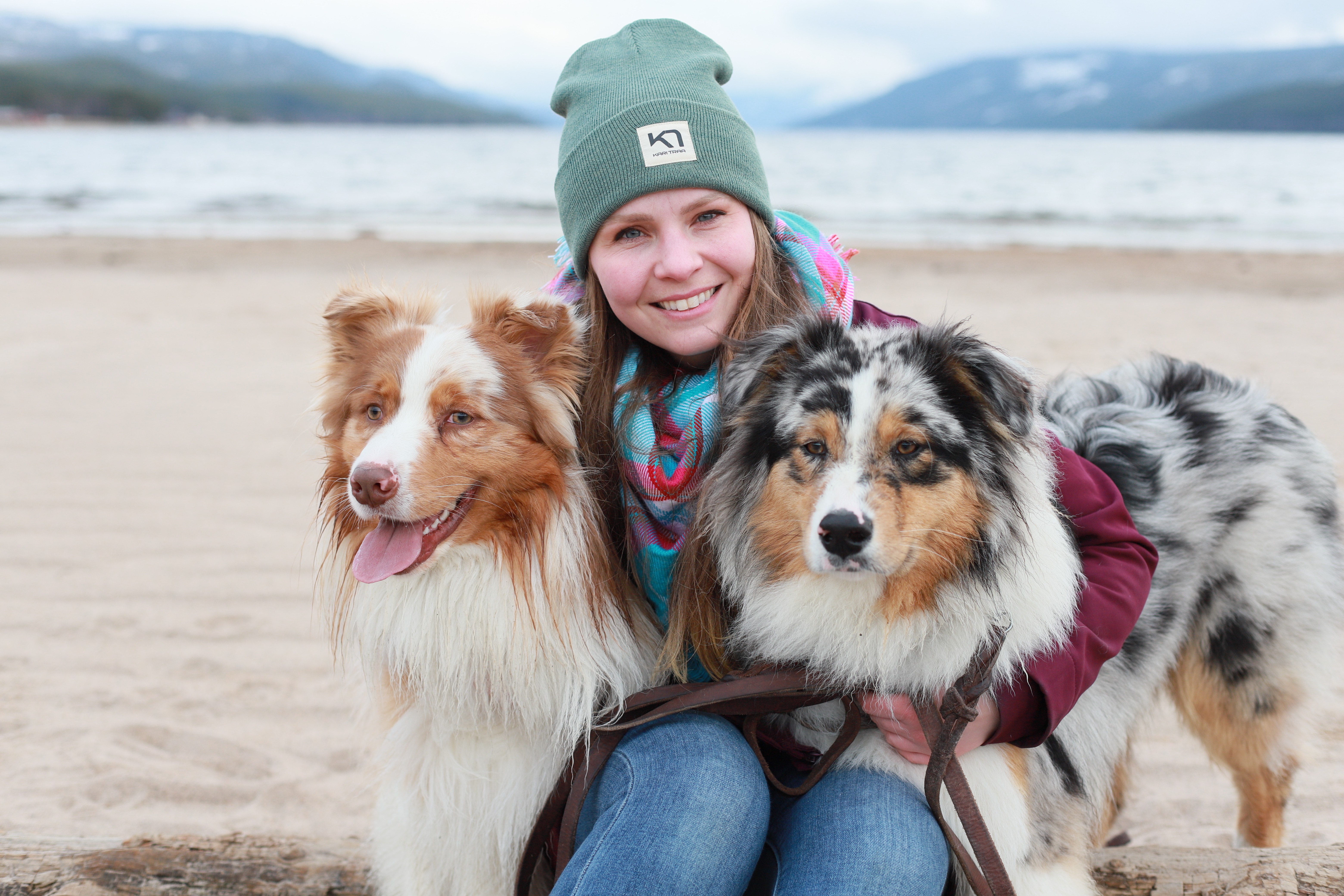 Kayla Buhler is sitting in the middle of two Australian Cattle Dogs, smiling at the camera.