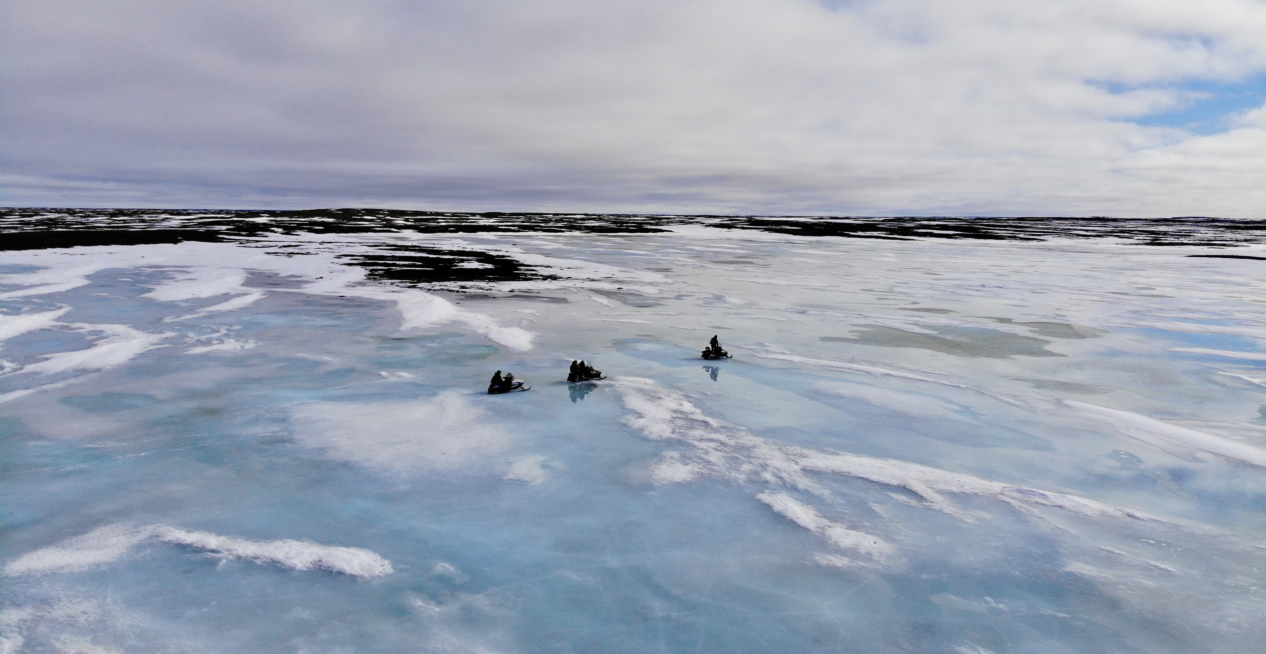 Three snowmobiles on a vast icy landscape