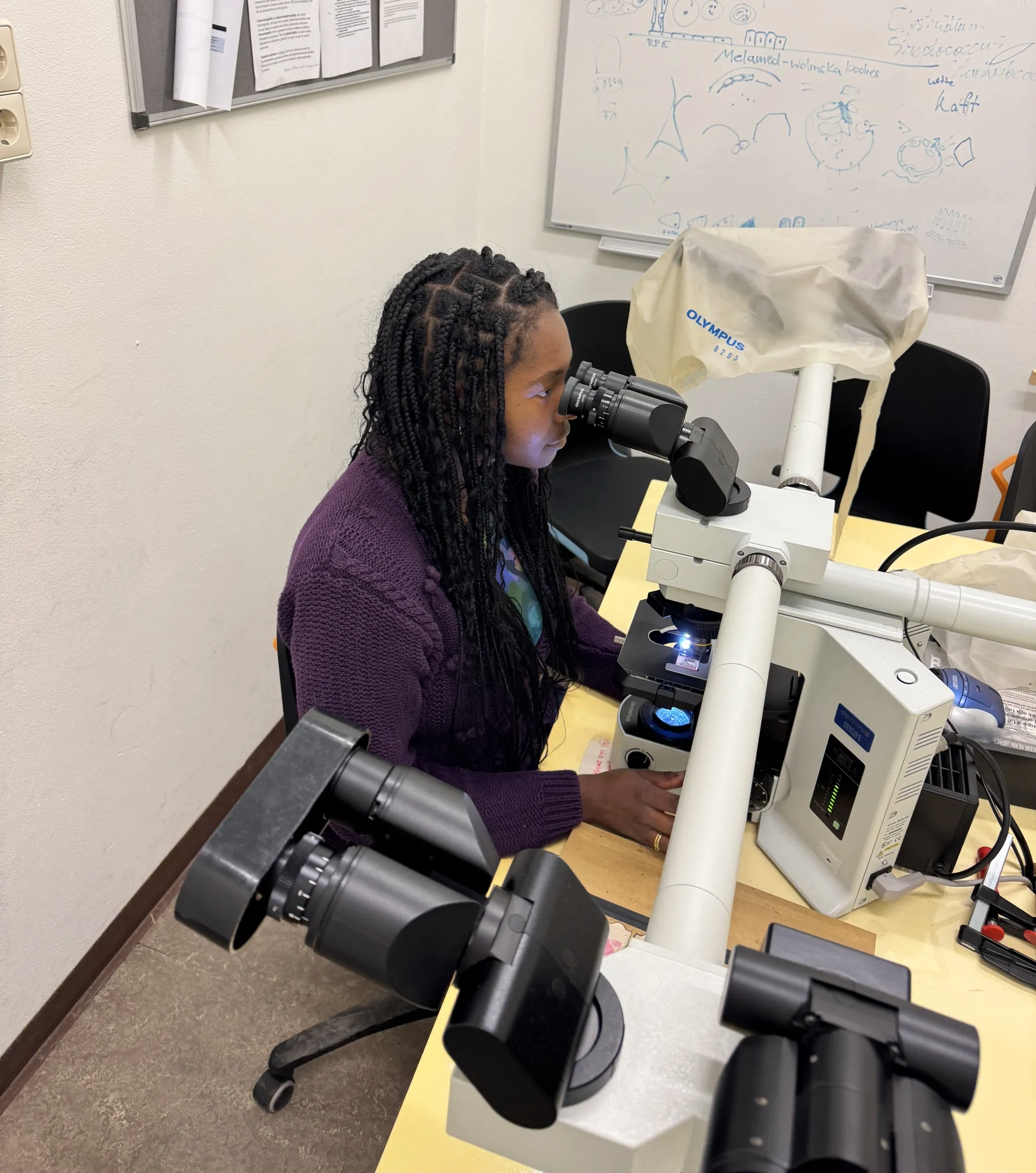 Victoria is seated at a table and looking through a microscope.