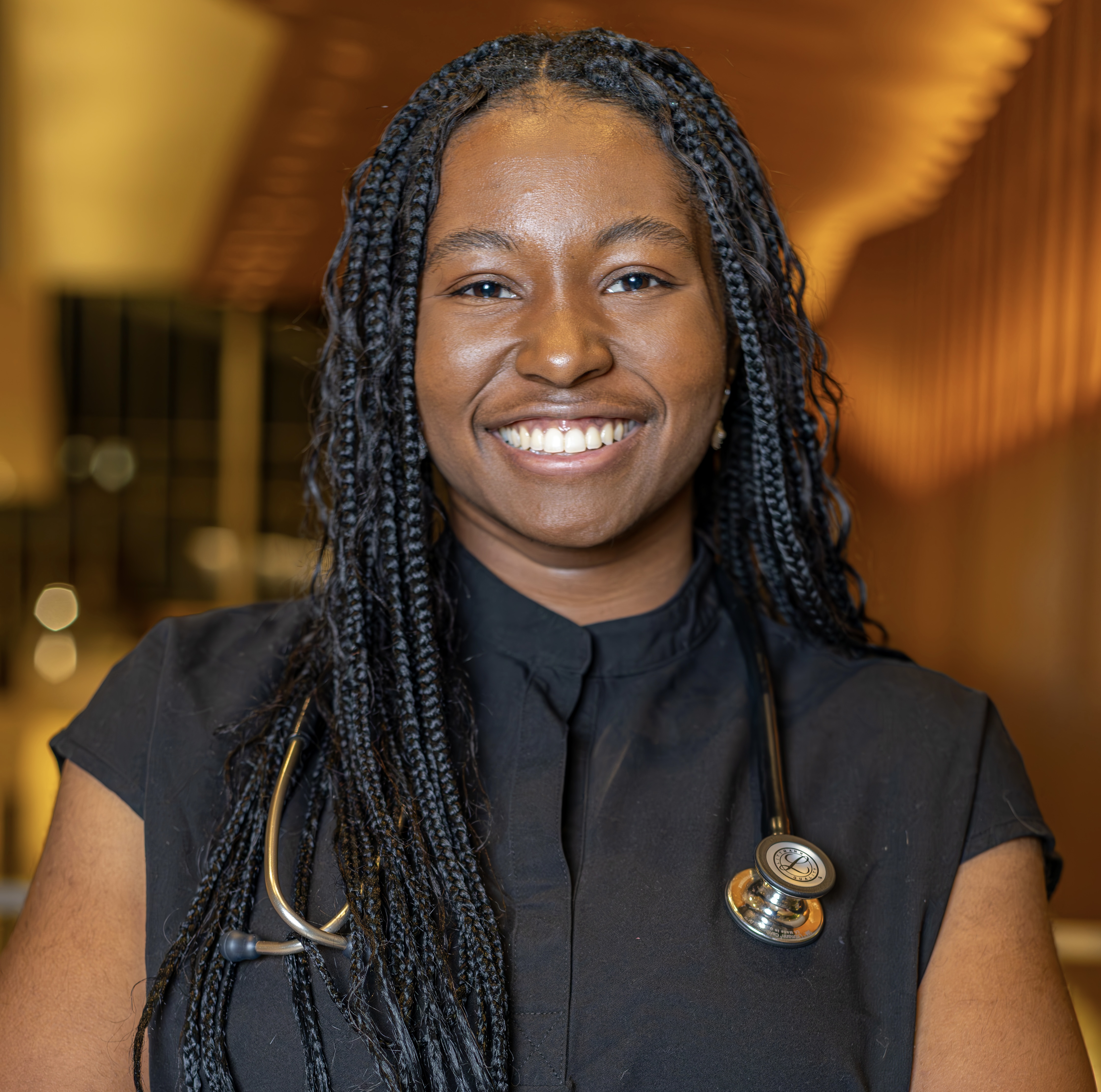 Victoria Priester wearing a black scrub top and stethoscope, smiling at the camera.