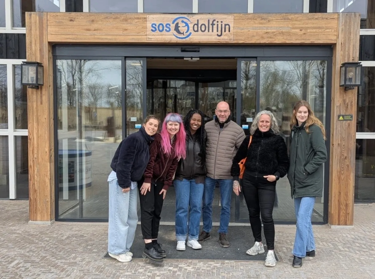 A group of six people smiling at the entrance of a building called "SOS Dolfijn".