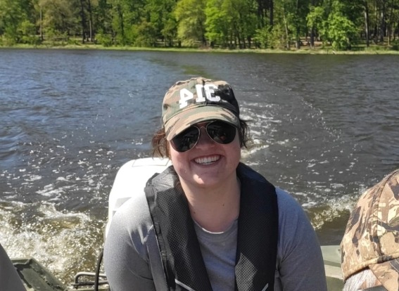 Anna is wearing a hat while riding in a boat and smiling at the camera.