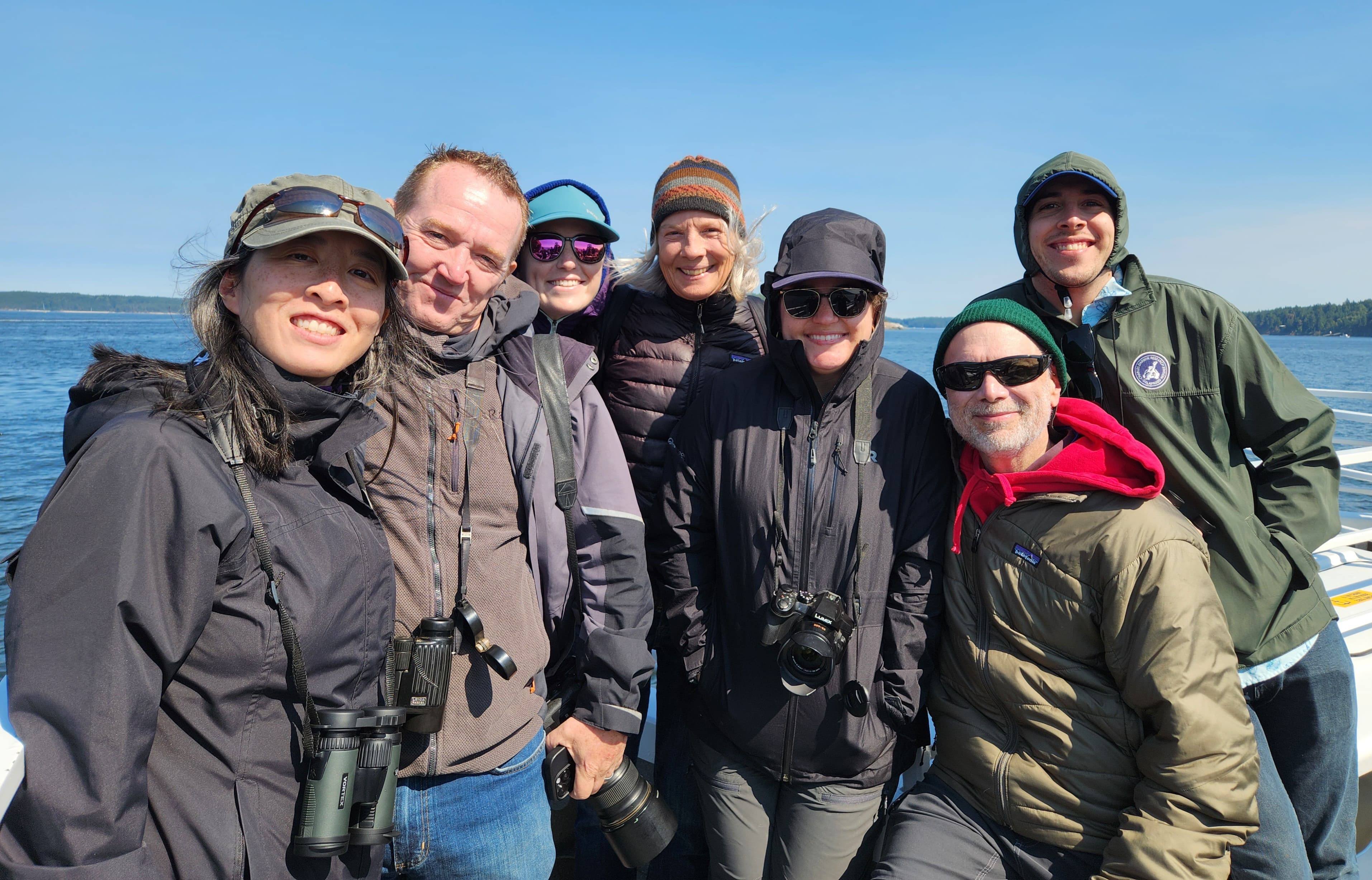 A group of seven people smiling with the ocean in the background