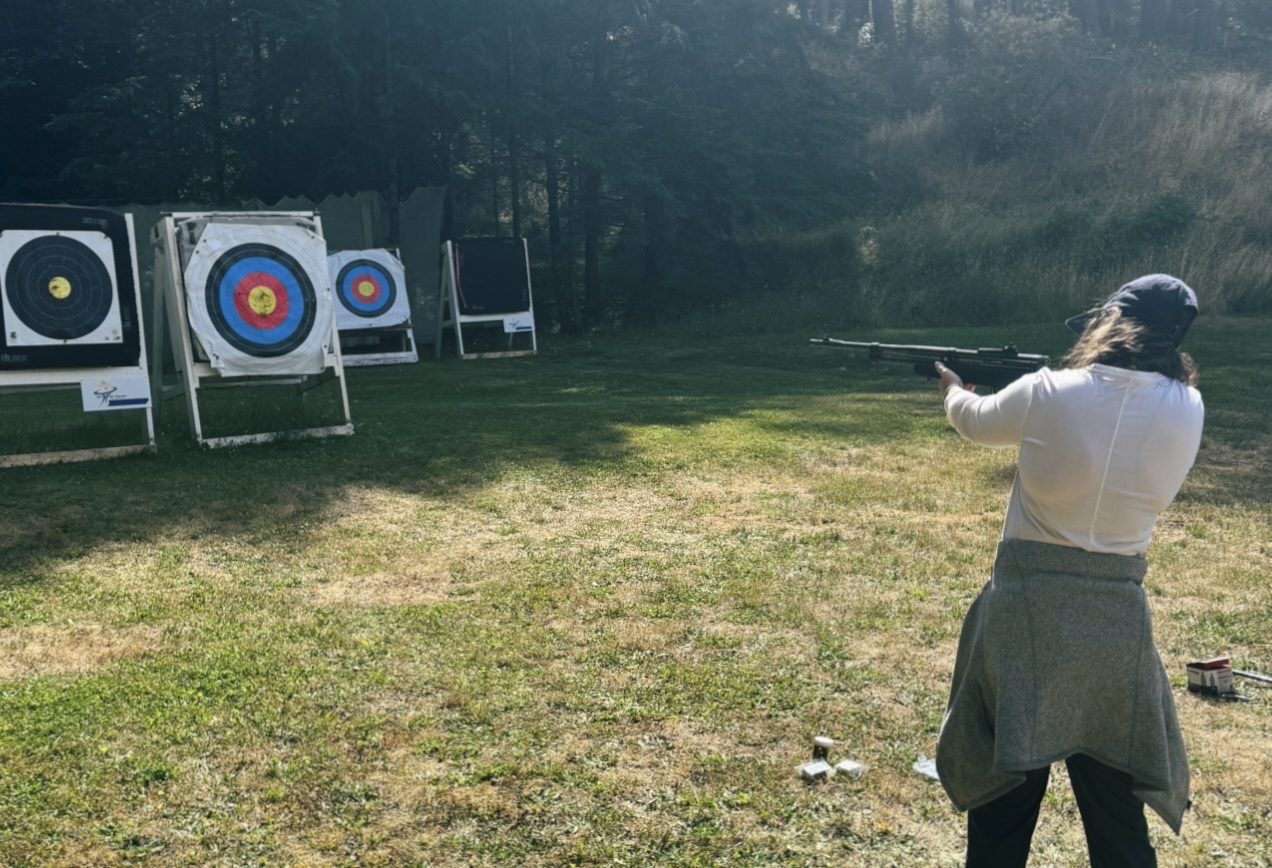 Shayna is outside aiming a dart gun at targets as the sun shines.