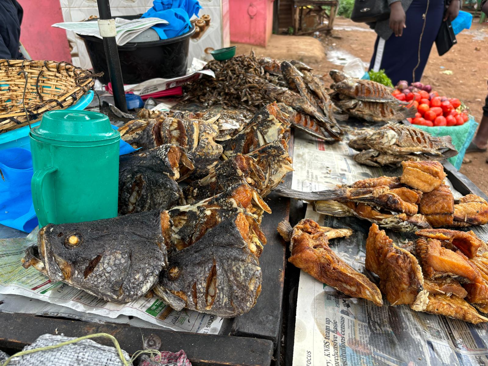 Fried Nile perch and tilapia sitting out on a table for sale in an outdoor market.