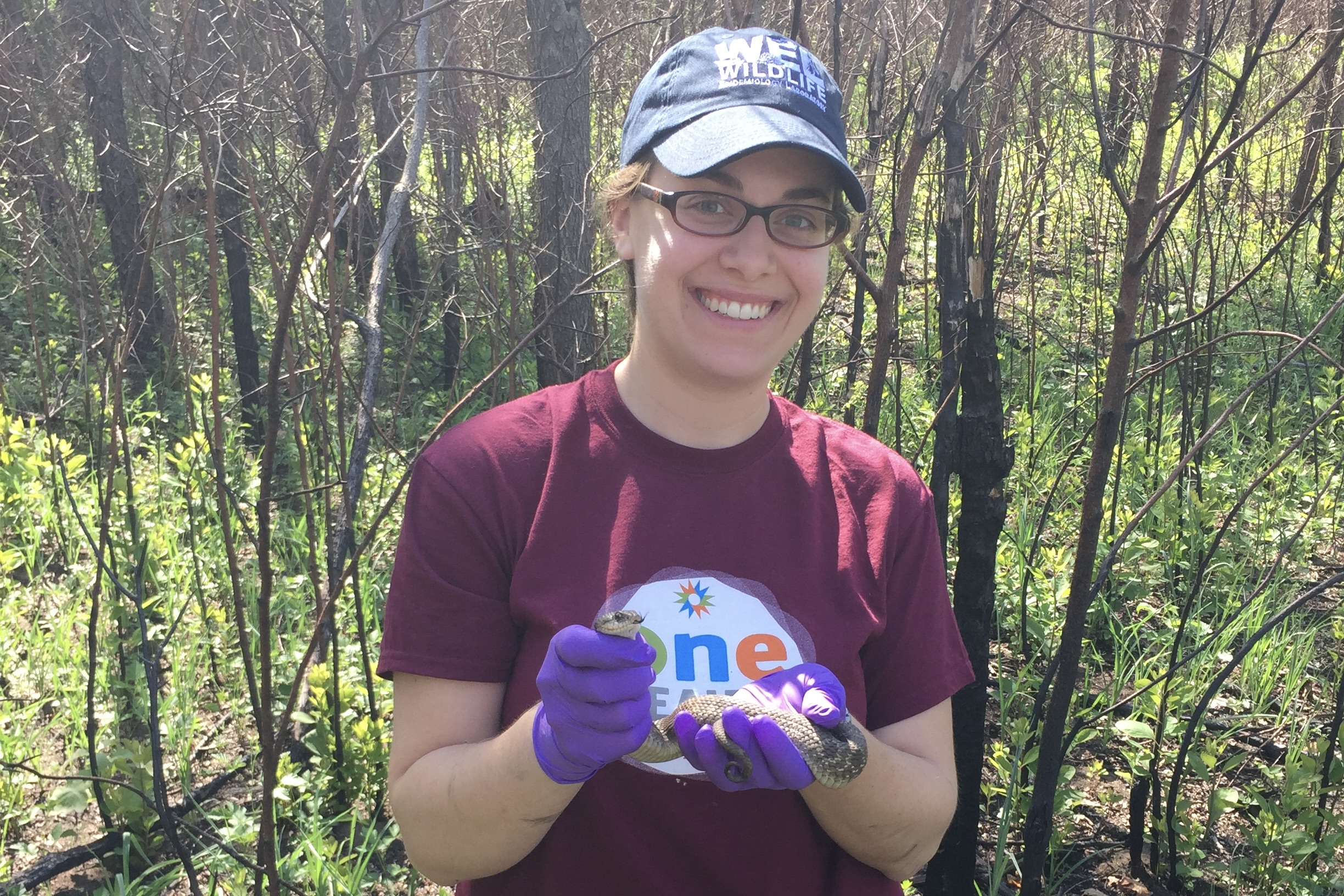 Dr. Haynes is in the forest while holding a snack and smiling at the camera.
