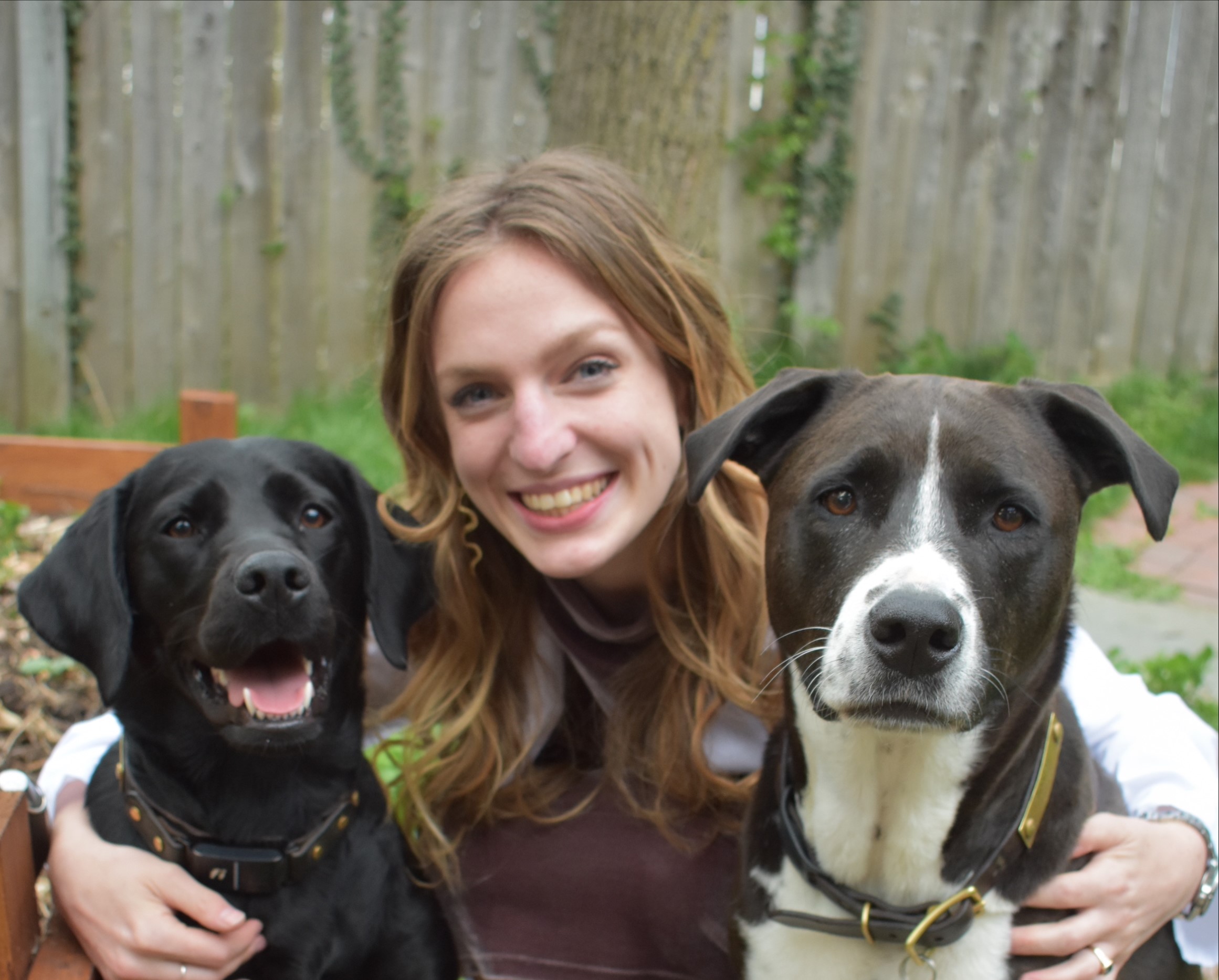 Emma is smiling, sitting in the middle of two dogs.