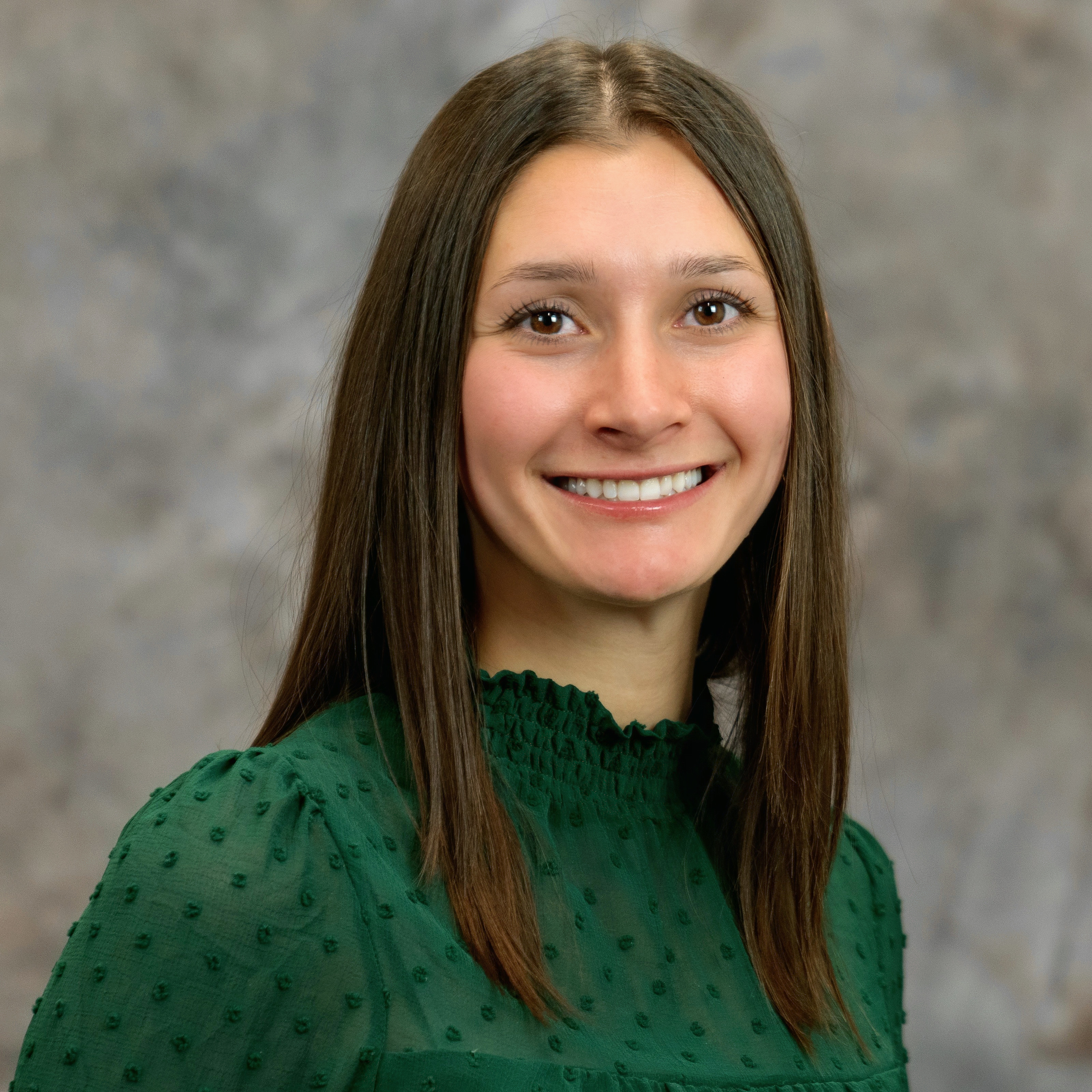Katie is smiling at the camera wearing a green shirt with a grey background.