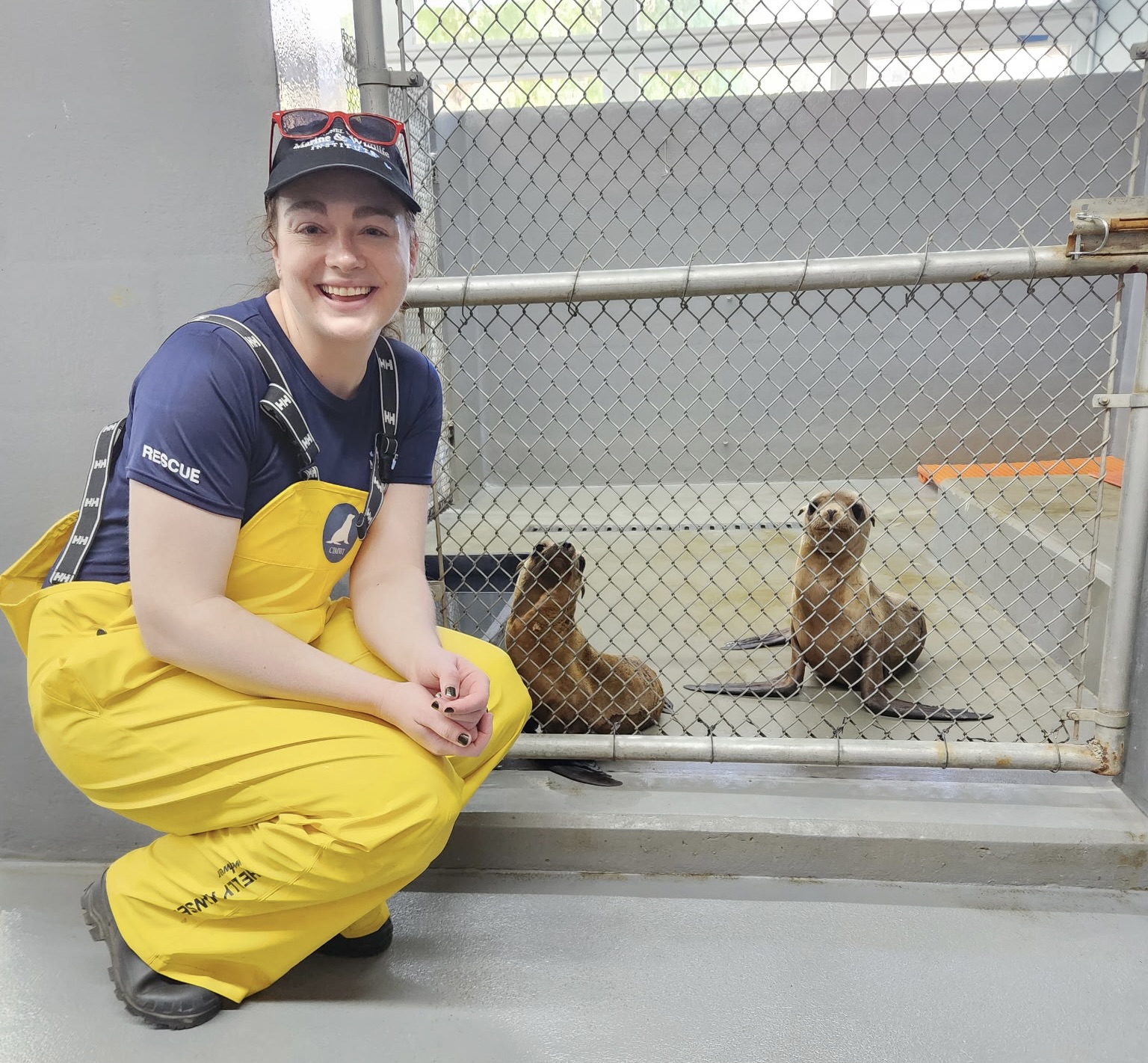 Kathleen smiles next to an enclosure with two sea lions inside.