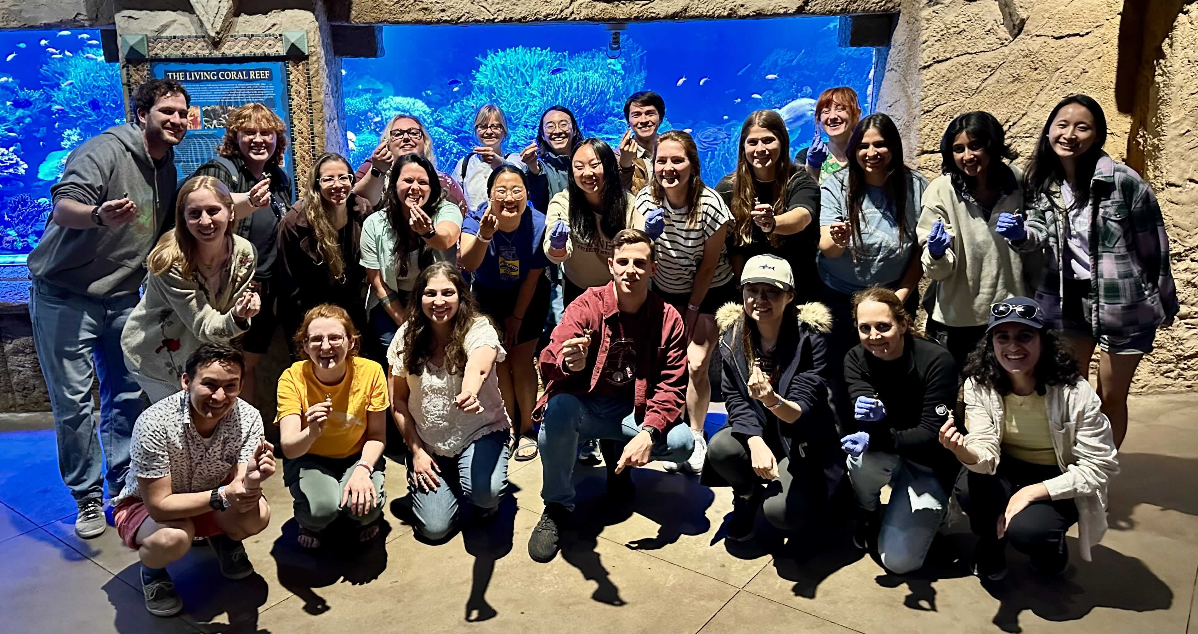 A group of people smiling in front of an aquarium display.