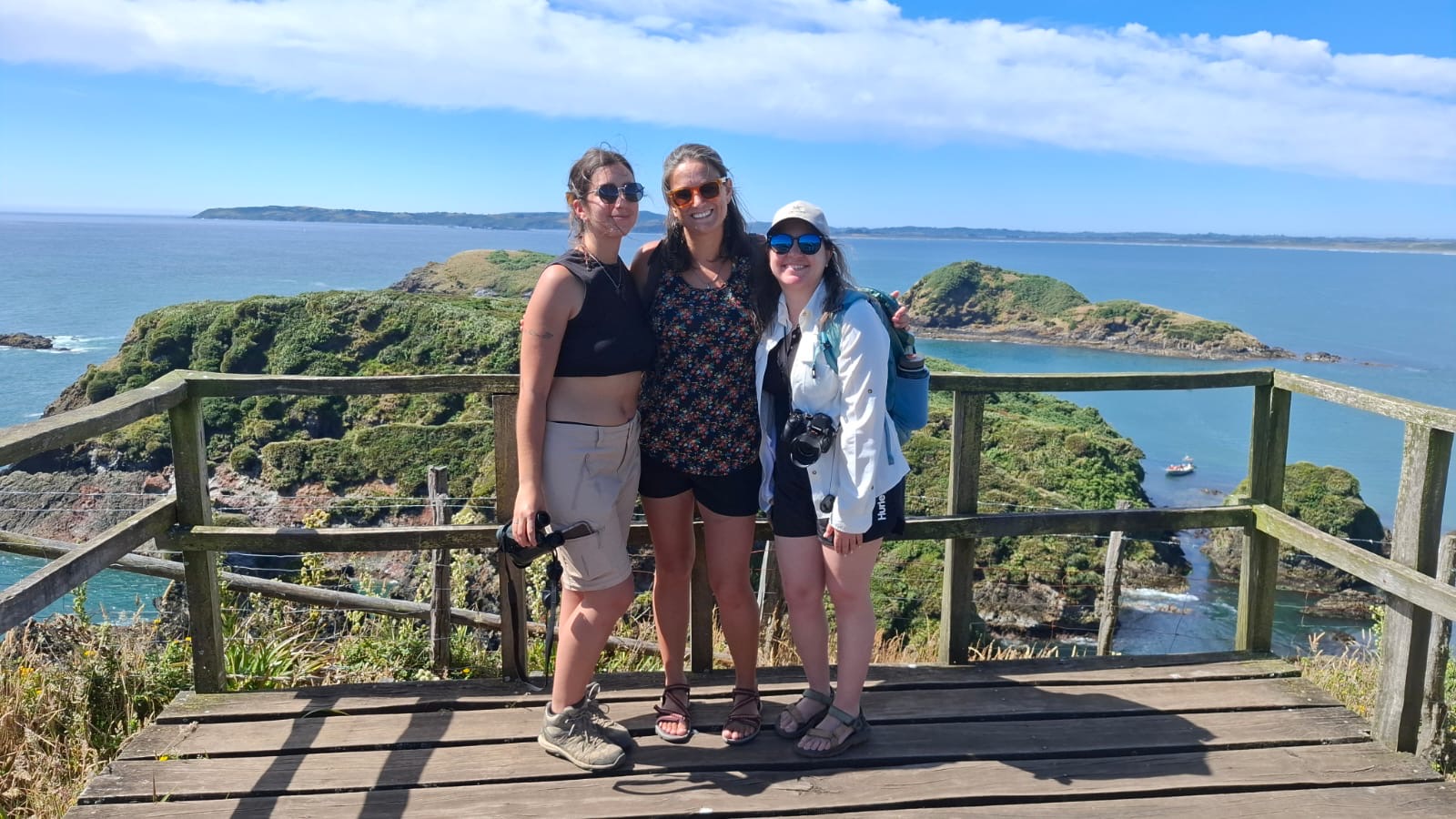 Three people smiling at the camera with an ocean landscape and blue skies in the background.