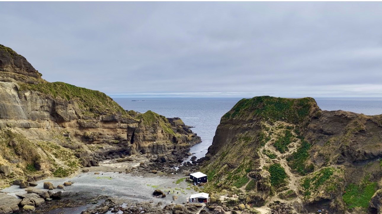 Rocky coastal cove bordered by steep, grass-covered cliffs