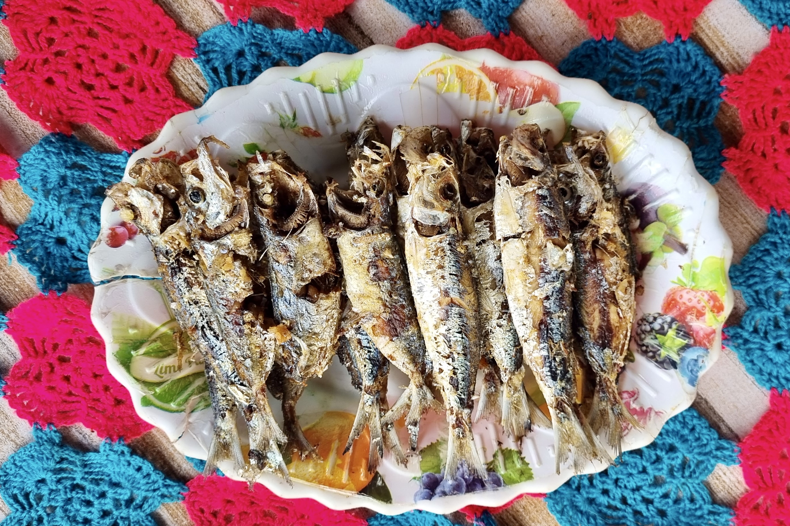 A plate of fish sits on a colorful table cloth.
