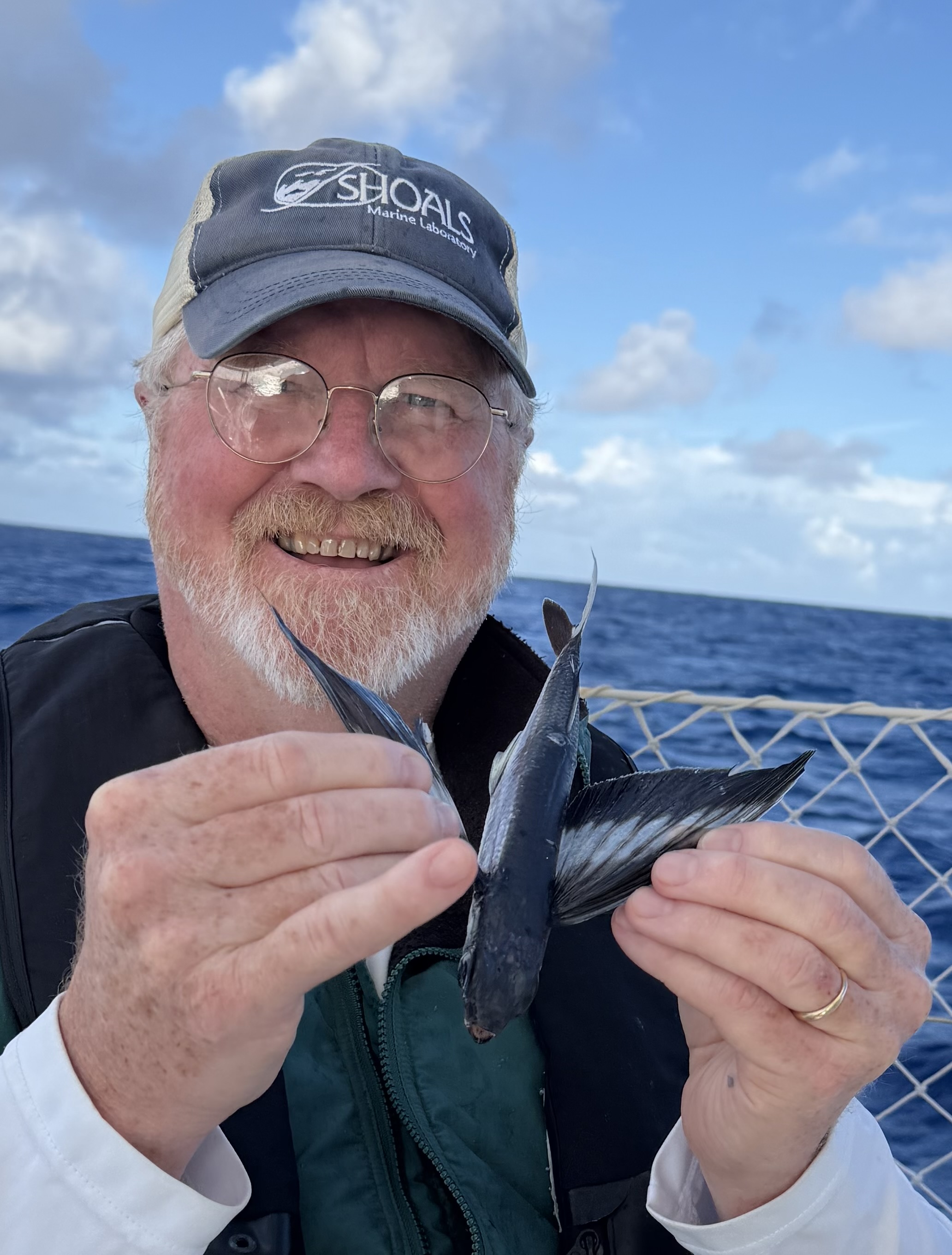 Rod smiling while holding a fish with the ocean in the background.