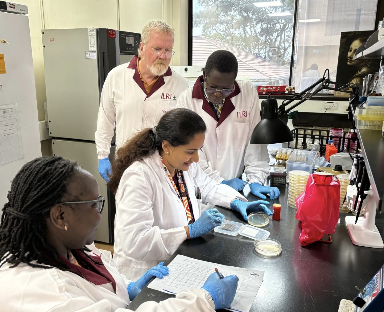 Rod Getchell is looking over the shoulder of several students working at a lab bench.