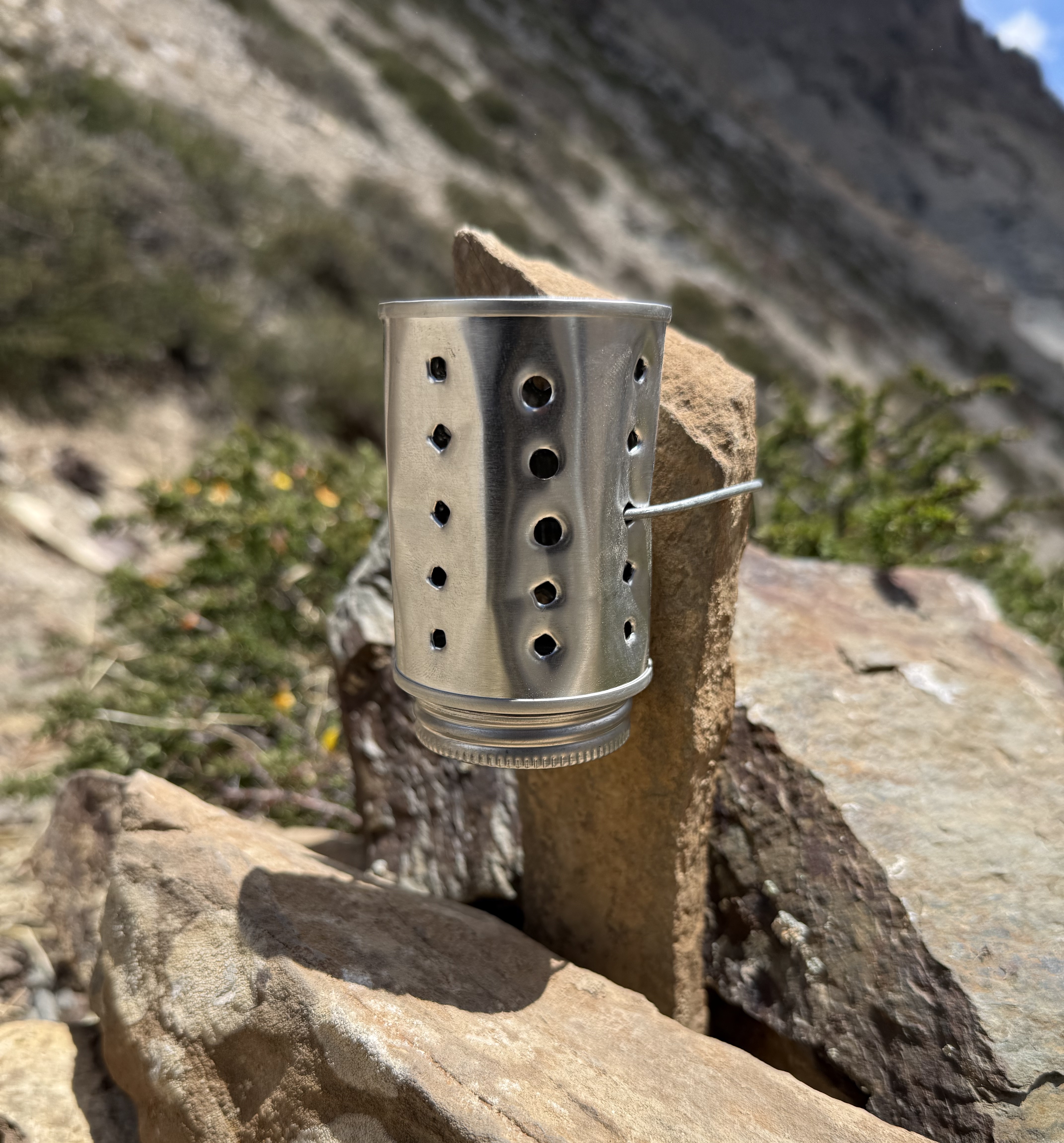 A small metal vial with holes attached to a rock