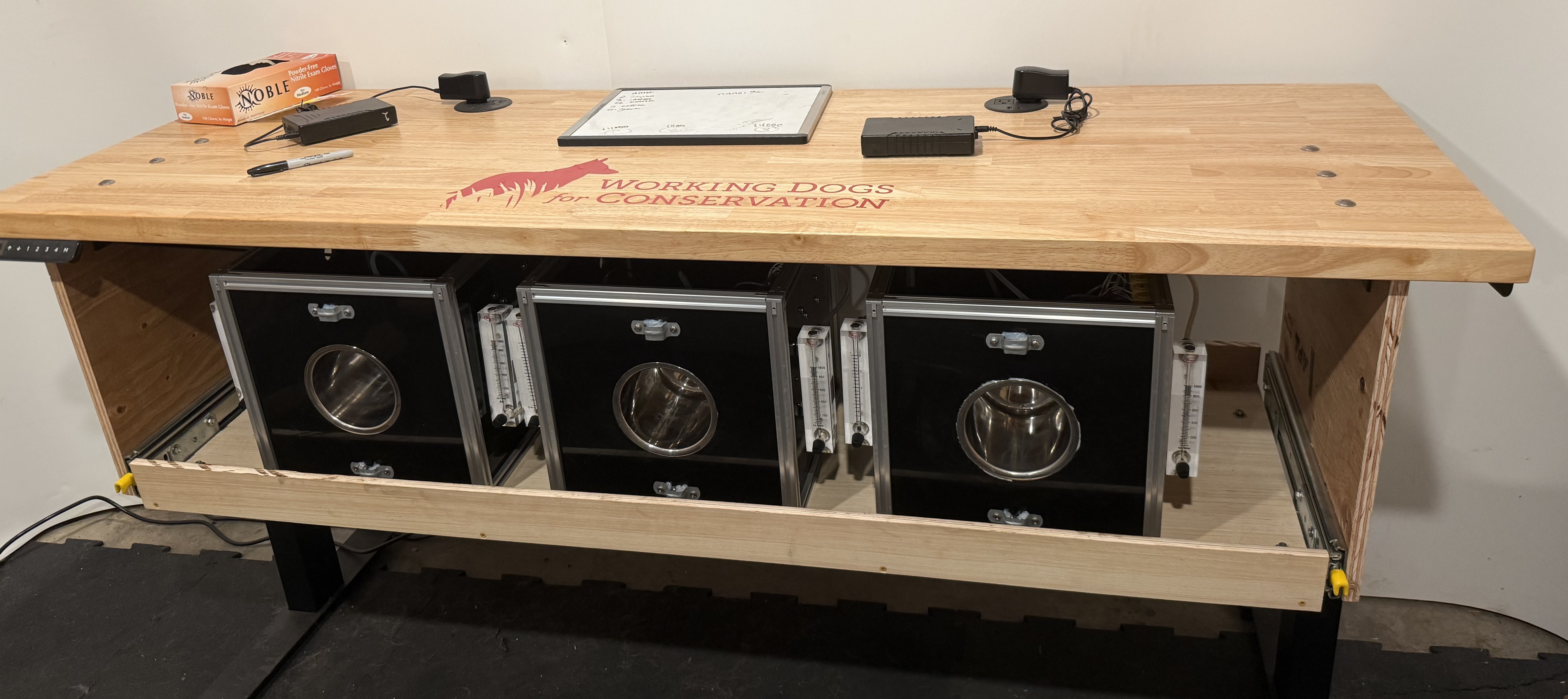 Three black boxes mounted in a wooden structure labled Working Dogs for Conservation