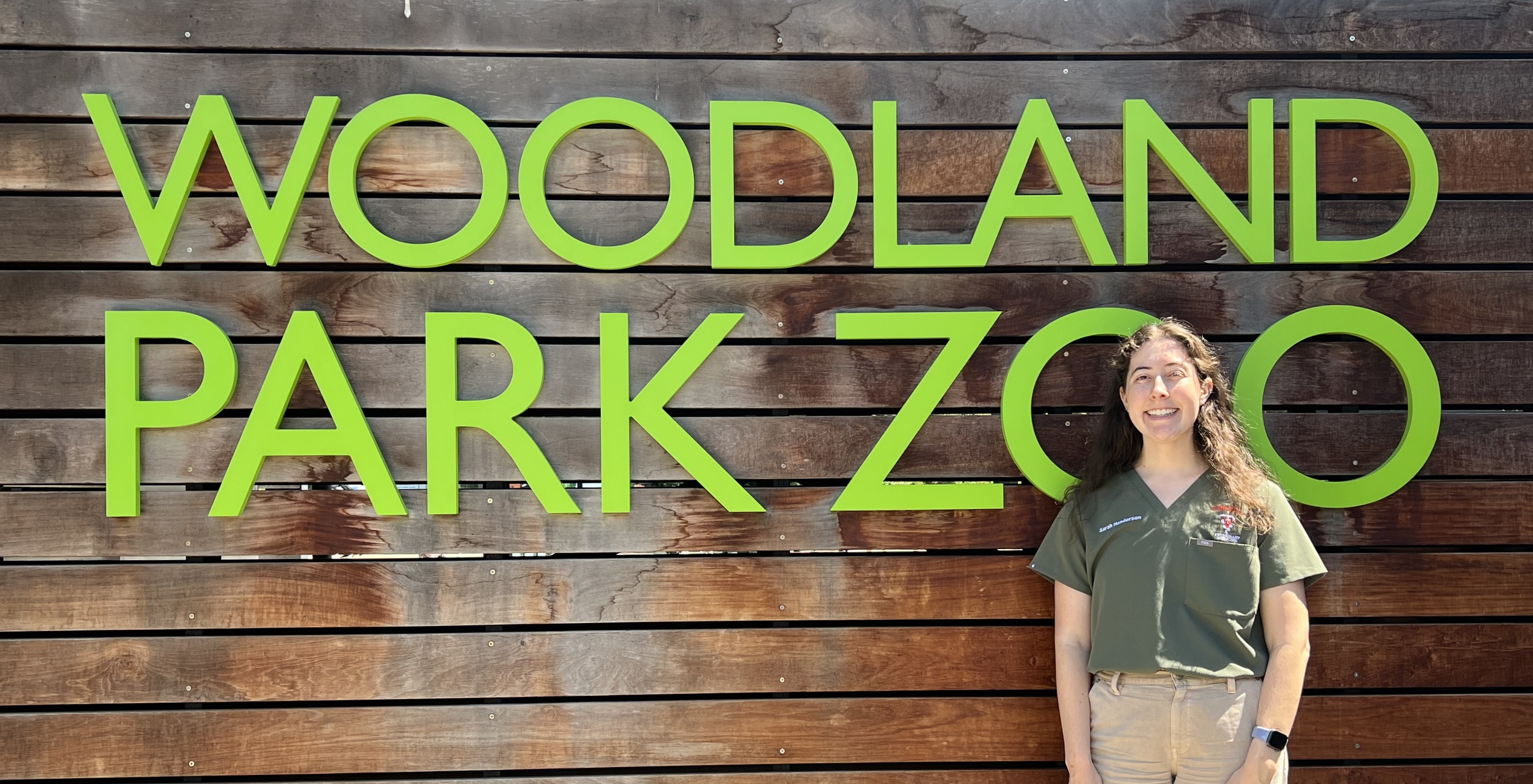 Sarah stands in front of a sign that says Woodland Park Zoo