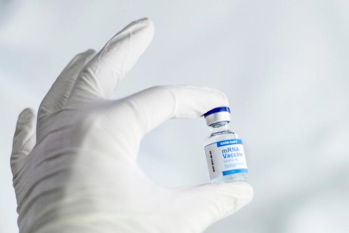 A white-gloved hand hold a vaccination bottle with the writing "mRNA Vaccine", with a white background.