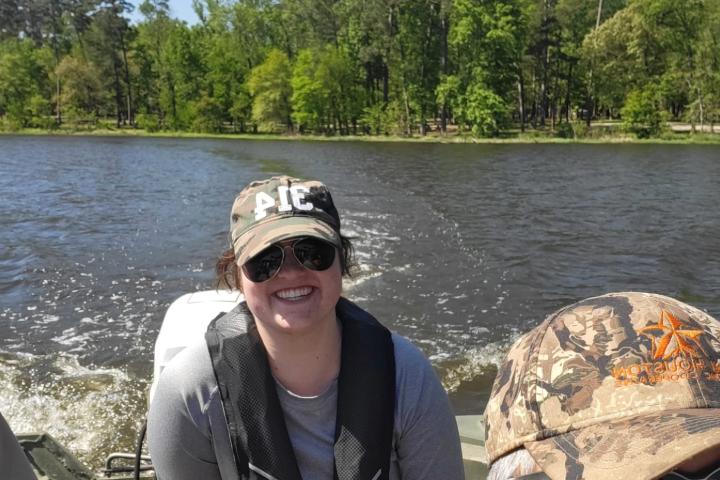 Anna is wearing a hat while riding in a boat and smiling at the camera.