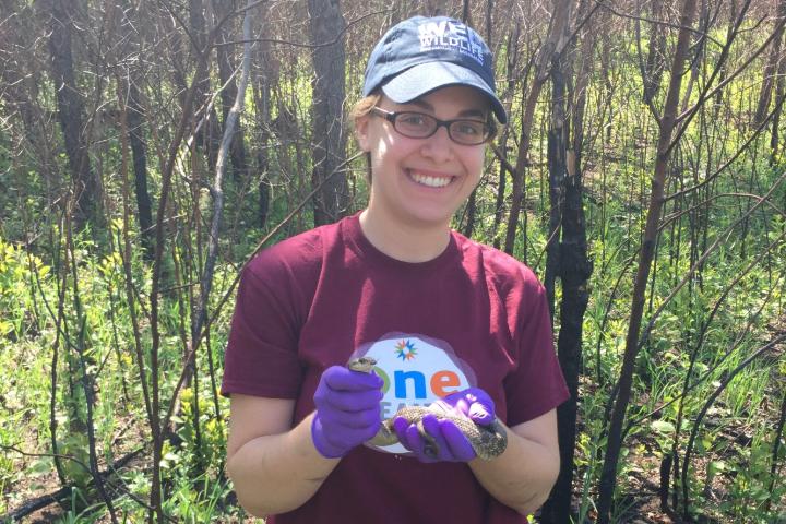 Ellen is in the forest while holding a snack and smiling at the camera.