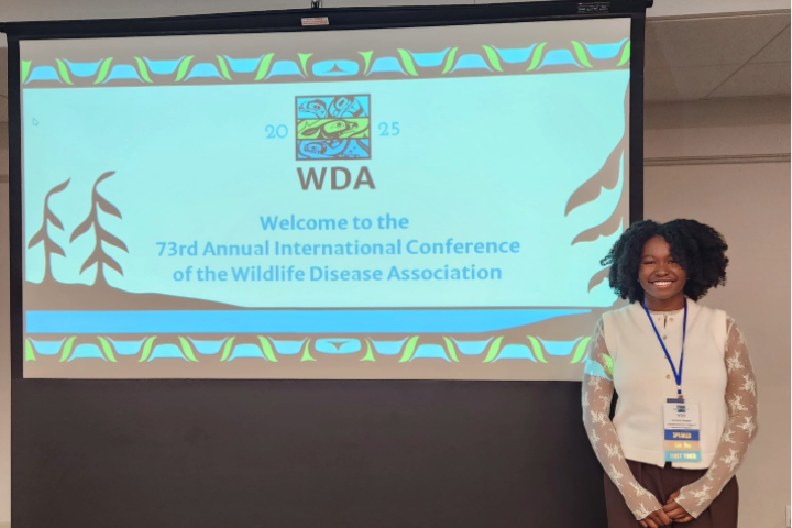 Victoria stands next to a large screen with a PowerPoint slide that says "WDA Welcome to the 73rd Annual International Conference of the Wildlife Disease Association"