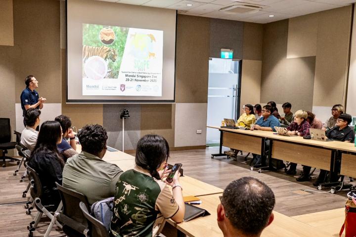 Dr. Carmen Smith stands next to a projector screen showing a slide while a group of people look on.