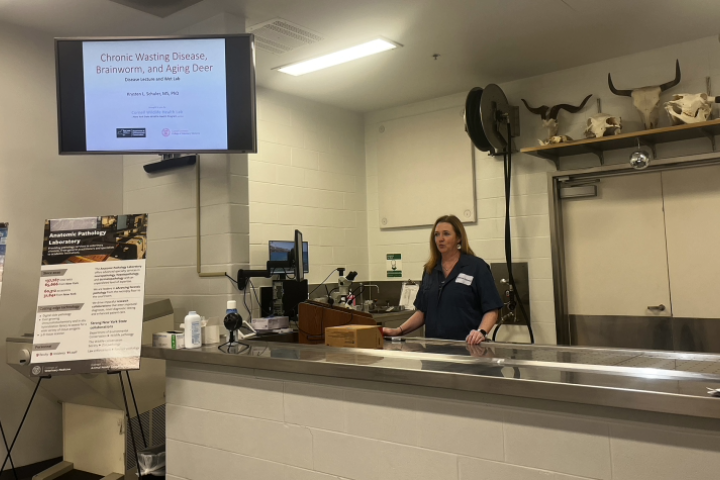 Krysten Schuler stands at a steel table in a lab like setting while speaking.