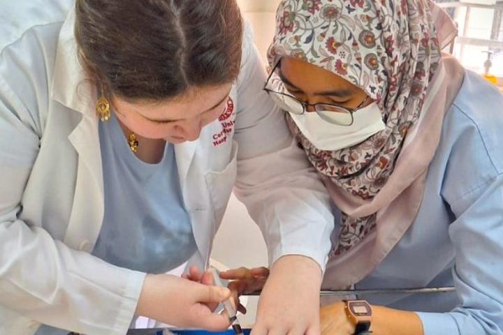 Two women are bent over a lab table, performing a procedure with a needle and syringe.