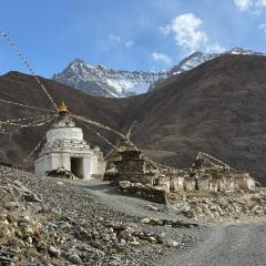 A small building with rock walls and structures with large mountains behind