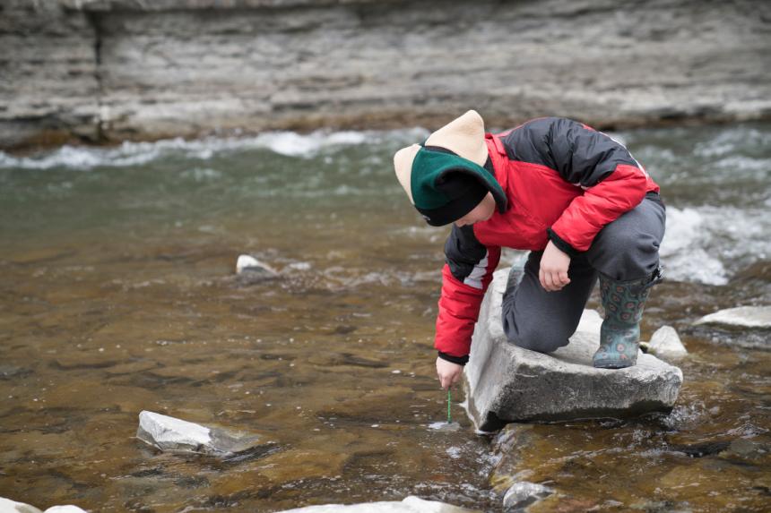 Student kneeling on rock in stream