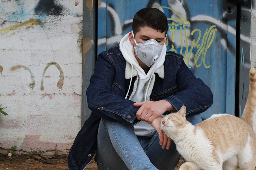 Person wearing face mask sitting outside with cat