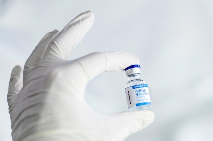 A white-gloved hand hold a vaccination bottle with the writing "mRNA Vaccine", with a white background.