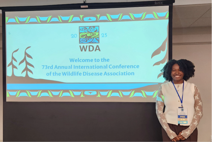 Victoria stands next to a large screen with a PowerPoint slide that says "WDA Welcome to the 73rd Annual International Conference of the Wildlife Disease Association"