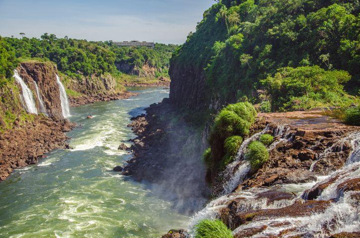 A waterfall falling into a river surrounded by a lush landscape.