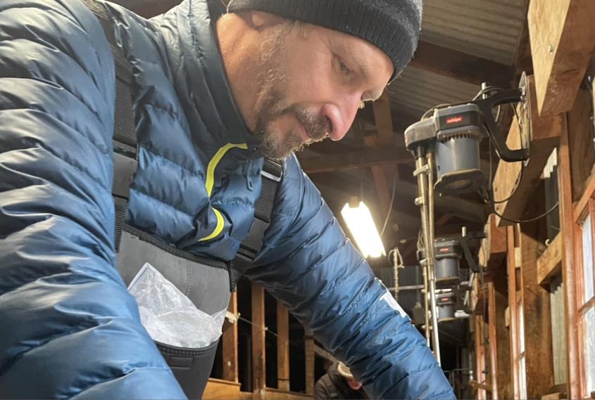 Jan Lovy wearing a coat and coveralls, looking down in a rural lab setting.