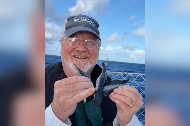 Rod smiling while holding a fish with the ocean in the background.